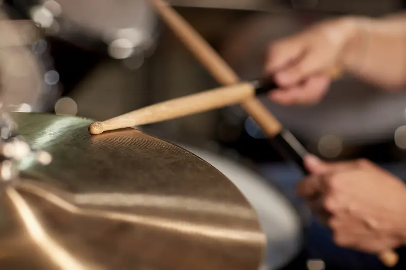 Baguette de batteur posée sur une cymbale, les mains floues en arrière-plan