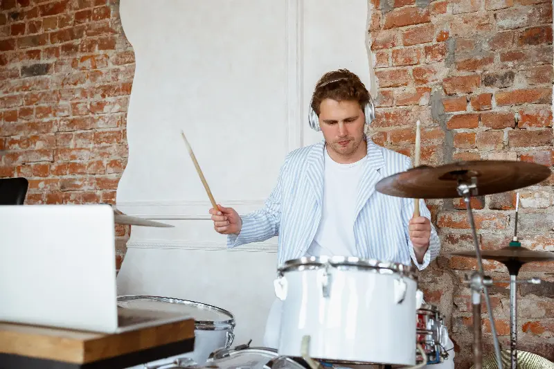Batteur au casque qui joue sur une batterie blanche, un ordinateur portable ouvert devant lui