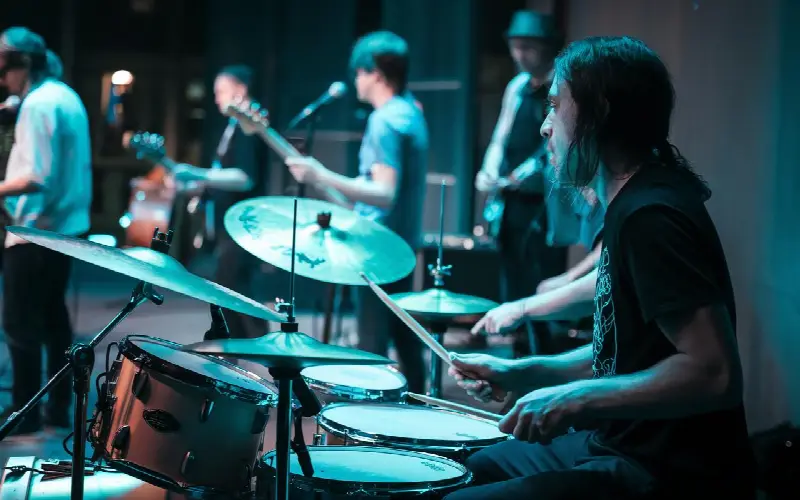 Batteur aux cheveux longs derrière sa batterie, sur scène avec son groupe