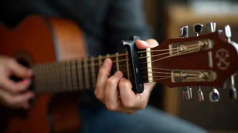 Capodastre à pince serré sur le manche d'une guitare folk, juste derrière une frette