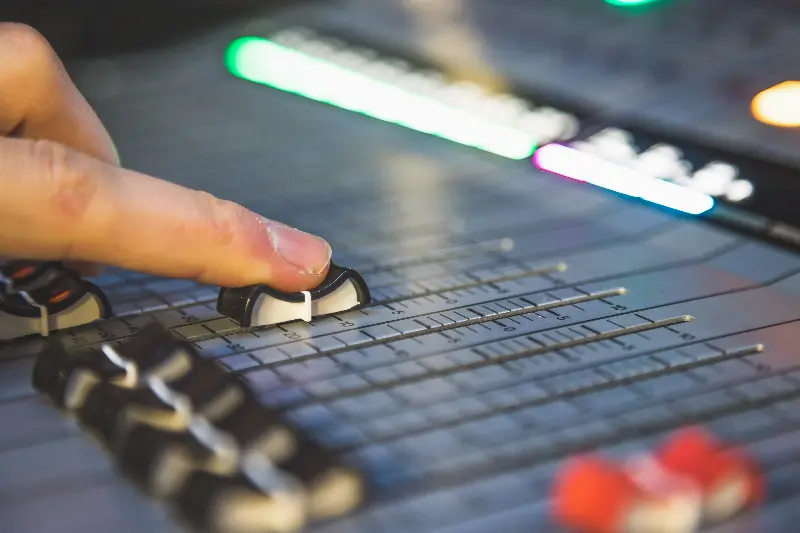 Doigt qui pousse un fader sur une console de mixage éclairée