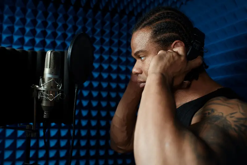Homme ajustant son casque face à un micro de studio et son filtre anti-pop, dans une cabine tapissée de mousse acoustique bleue