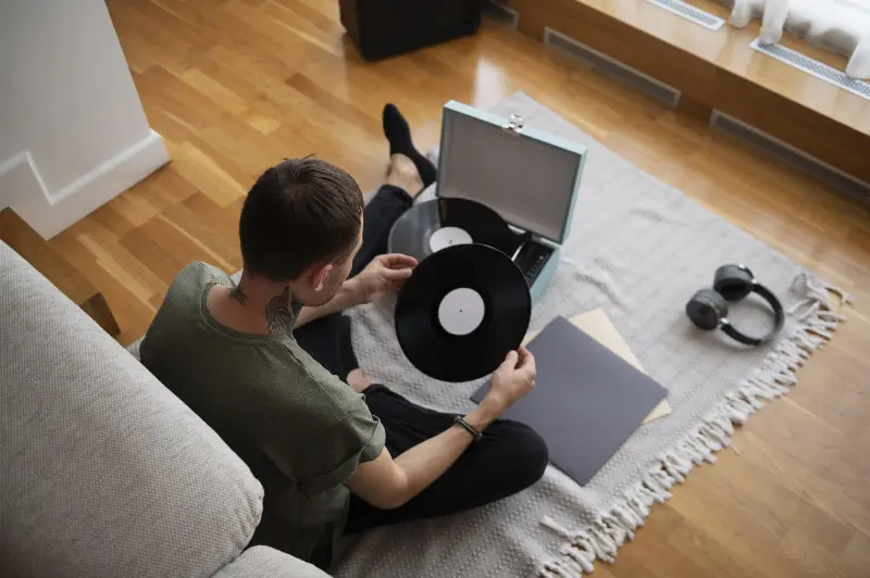 Homme assis sur un tapis, un disque vinyle en main, devant une platine valise ouverte et un casque