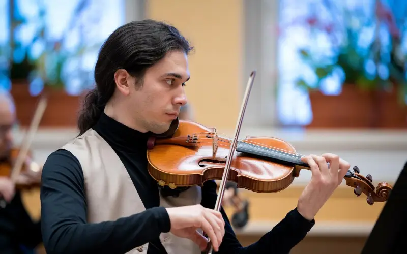Violoniste d'orchestre jouant archet sur les cordes, un autre musicien flou à côté de lui