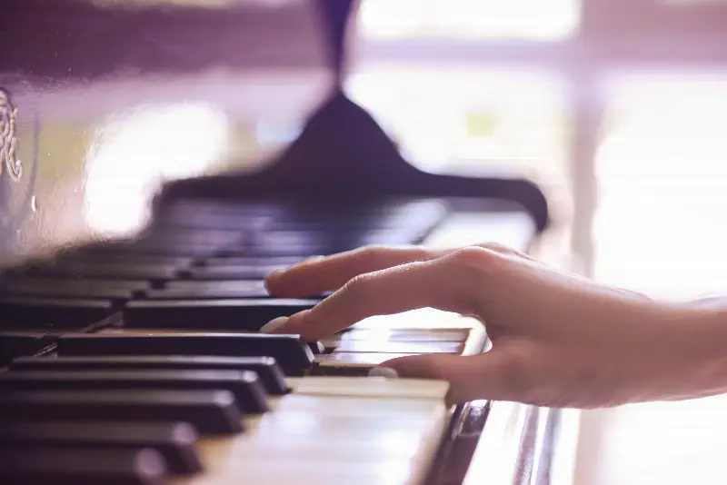 Main d'une pianiste posée sur les touches noires et blanches d'un piano, vue de profil en lumière douce