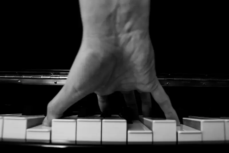 Main posée sur un clavier de piano, doigts écartés sur les touches blanches, en noir et blanc