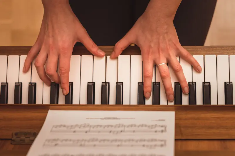 Mains posées sur le clavier d'un piano en bois, vues de dessus, devant une partition