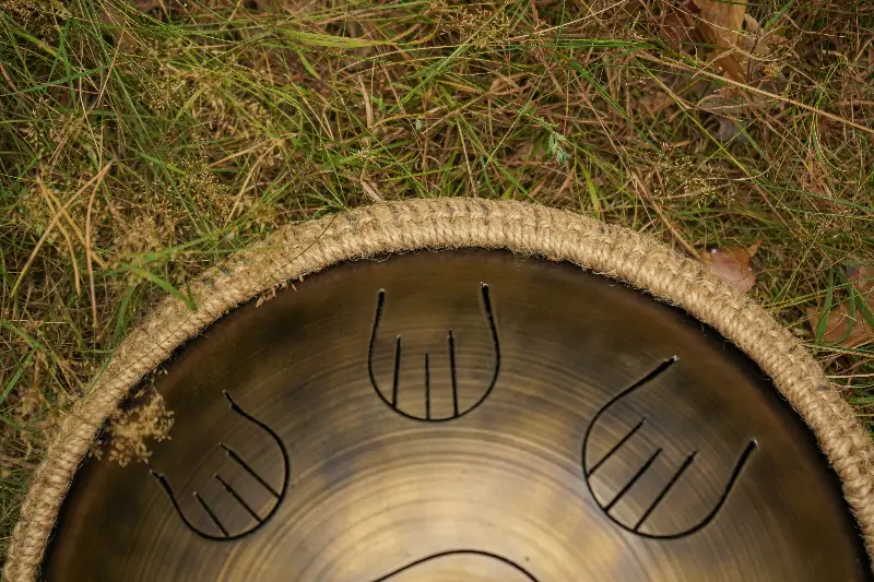 Tongue drum en acier patiné aux languettes découpées, posé dans l'herbe