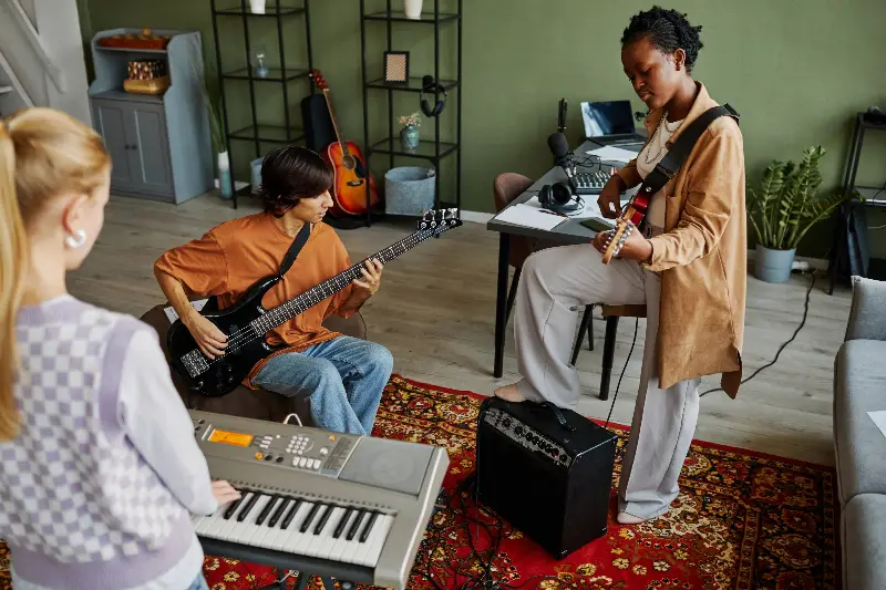Trois jeunes musiciens répètent dans un salon : clavier, basse et guitare électrique branchée sur un petit ampli