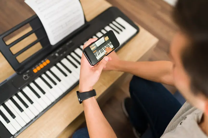 Une personne tient un téléphone qui affiche une leçon de piano, au-dessus d'un clavier électronique avec une partition